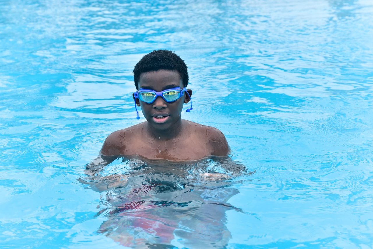 A young boy happily swimming in a bright turquoise pool, enjoying a sunny day.