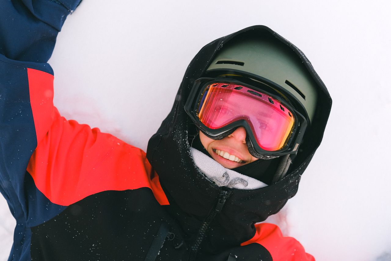 A joyful snowboarder wearing a helmet and goggles relaxing on a snowy slope.