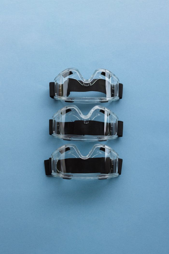 Three safety goggles arranged on a blue background, emphasizing PPE importance.