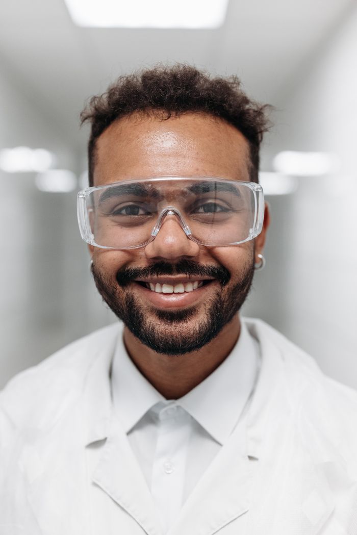 Portrait of a smiling doctor wearing safety goggles and lab coat in a bright hospital corridor.